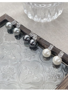 Three pairs of pearl earrings in white, grey, and black on a vintage glass tray