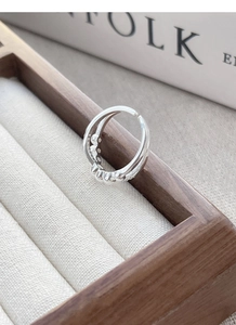 Macro detail of silver double-layer crisscross ring with polished beads on wooden stand