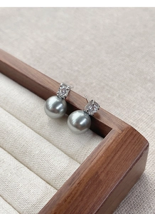 Detailed macro view of grey pearl earrings with sparkling zircon on a luxury wood display