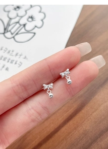 Close-up of S925 sterling silver bowknot bead earrings held on a finger for scale