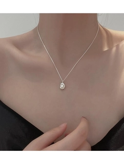 Detail of silver chain necklace featuring irregular metal pendant with a white pearl on neck