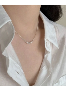 Detail of silver S925 necklace with three oval bean pendants on white shirt background