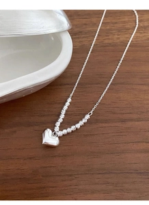 Detailed shot of polished silver heart pendant on a wooden table with shell decor