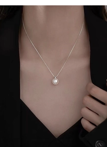 Close-up of a single 9mm white pearl pendant on a fine silver chain worn by a model