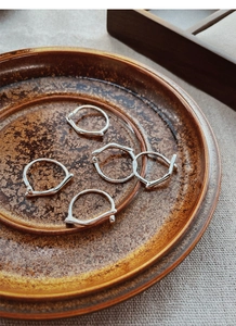 Artistic display of five irregular S925 sterling silver rings on a rustic ceramic plate
