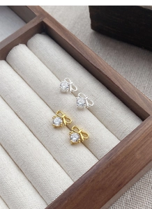 Macro detail of silver and gold bow stud earrings with sparkling cubic zirconia in a tray