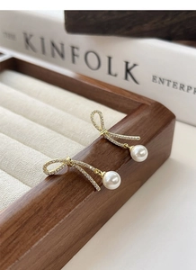 Close-up of golden ribbon bow earrings with round white pearl pendants on a wooden tray