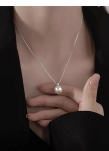 Close-up of elegant single pearl pendant on fine silver chain worn by a female model