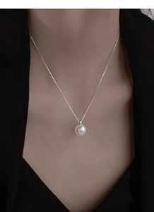 Close-up of a single white pearl pendant on a silver box chain worn on the neck