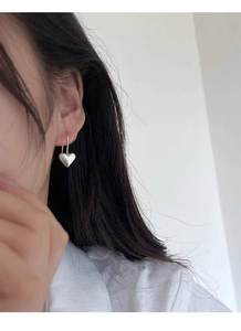 Dettaglio di orecchini a cuore in argento S925 indossati da una modella alla luce
