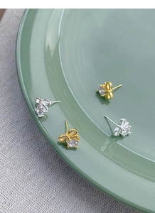 Macro shot of silver and gold bow stud earrings with zircon stones on a green plate