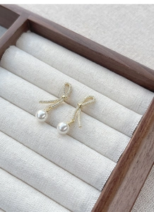 Detail of silver ribbon bow earrings with pavé crystals and elegant hanging white pearls
