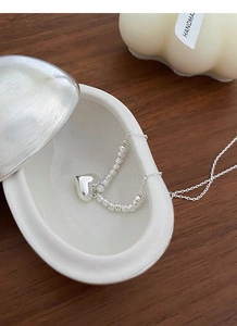 Close-up of S925 sterling silver heart necklace with beads in a white ceramic bowl