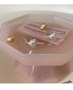 Dettaglio di orecchini a cuore bicolore in argento S925 su un vassoio decorativo rosa