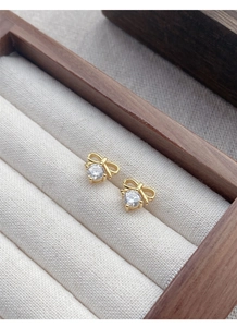 Close-up of golden bow-shaped S925 silver studs with a sparkling zircon center