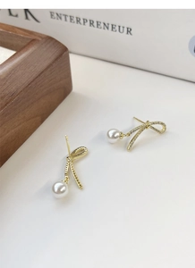 Close-up of gold bow earrings with pavé zircons and dangling lustrous white pearls