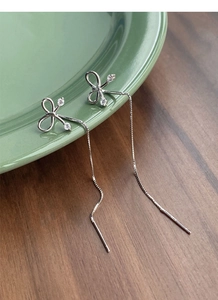 Detail of S925 sterling silver bow tassel earrings with sparkling crystals hanging on a tray