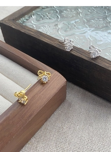 Detail of silver bow earrings with round zircon stones on a wooden display stand
