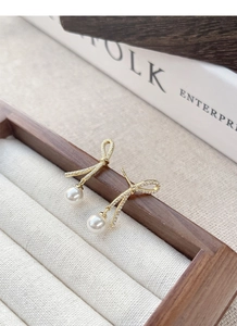 Close-up of gold bow earrings with pavé zircons and dangling pearls on display