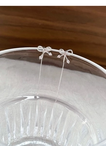 Detail of silver bow tassel earrings with pink zircons on glass edge, elegant long chains