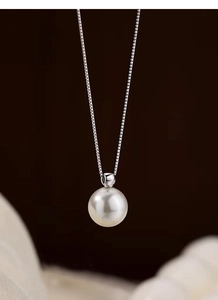Close-up of a lustrous white pearl pendant on a silver box chain with high-end texture