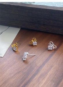 Macro detail of silver and gold bow earrings with zircon studs on wood background