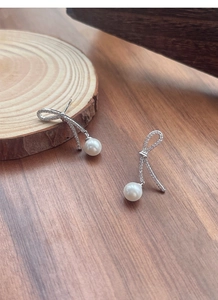 Macro detail of silver bow earrings with pavé zircons and dangling white round pearls
