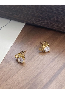 Detail of gold bow earrings with round zircon stones on a rustic wooden texture surface