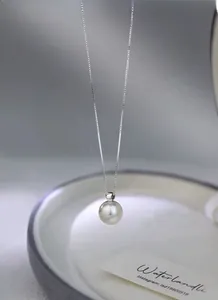 Macro shot of a single round white pearl pendant on a S925 silver box chain over ceramic