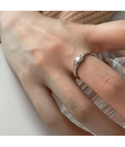 Irregular fluid silver ring with a sparkling round zircon shown on hand holding a glass