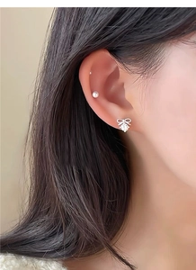 Close-up of silver bow stud earrings with sparkling zircon on a female model's ear