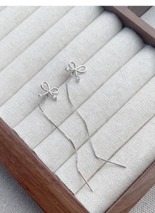 Close-up of S925 silver bow tassel earrings with small zircons on a beige velvet box