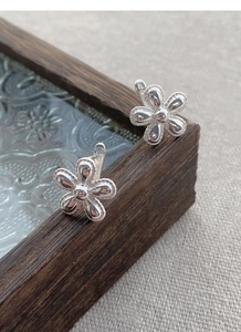 Macro detail of S925 sterling silver sunflower stud earrings on vintage glass and wood