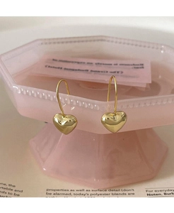 Dettaglio di orecchini a cuore dorati su un vassoio rosa con illuminazione soffusa