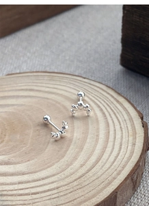 Macro shot of silver beaded crescent stud earrings with screw ball backings on wood
