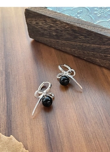 Close-up of S925 silver bow earrings with black agate pearls on a wooden surface