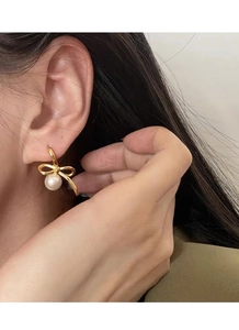 Detail of bow-shaped gold stud earring with a white round pearl drop on ear