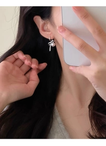 Detail view of a silver bow earring with a round white pearl on a model in close-up shot