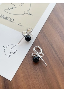 Detailed shot of S925 silver bow earrings with black onyx bead on a wooden background