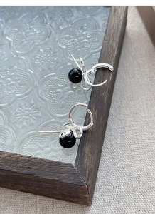 Close-up of S925 silver bow earrings with black onyx beads on a vintage fabric tray