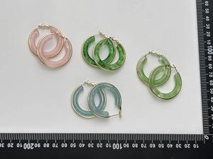 Detailed view of four colorful resin hoop earrings in pink green and blue with gold trim