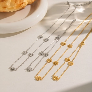 Elegant gold and silver daisy necklaces set on white tray with warm ambient lighting