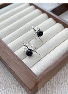 Detailed close-up of S925 silver bow earrings with black onyx bead in jewelry box