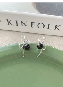 S925 silver bow earrings with black agate beads on a ceramic tray with a book