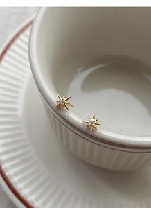 Detail view of gold starburst earrings with white zircon on a vintage white cup edge