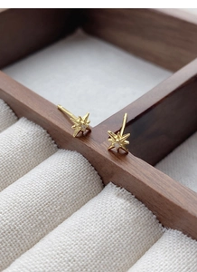 Macro detail of gold star earrings with tiny zircon stone in a wood jewelry box