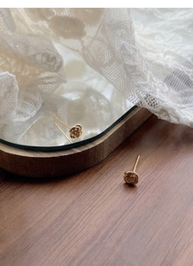 Détail de boucles d'oreilles roses dorées avec texture de pétales sur fond de dentelle