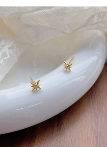 Macro detail of gold-plated star earrings with white zircon on elegant lace background