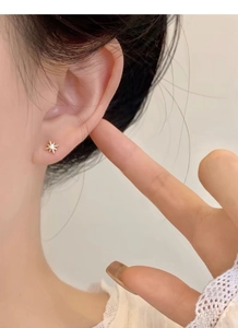Macro close-up of a minimalist gold starburst stud earring worn on a model's ear lobe
