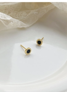 Macro shot of gold Roman numeral earrings with black inlay on elegant lace background